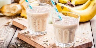 Two glasses filled with peanut butter banana smoothie with a white and blue striped straw.